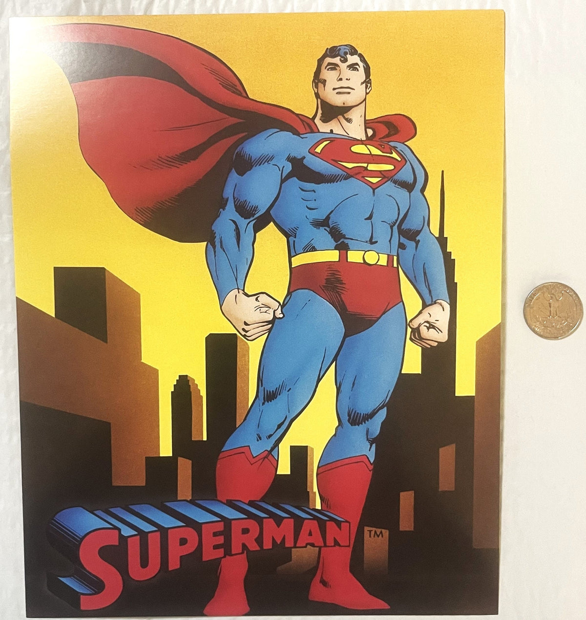 Vintage Superman lobby card featuring the superhero in blue suit and red cape standing over a cityscape, with a coin placed r