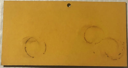 Faded yellow advertising card with two faint circular marks and a hole punched at top center