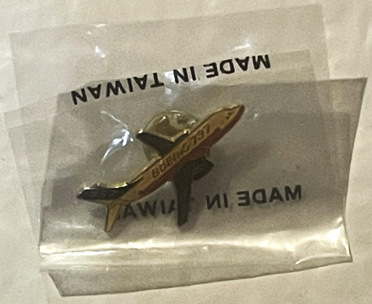Sealed plastic bag containing a gold and brown Boeing 737 enamel lapel pin, text visible on bag reads "MADE IN TAIWAN" and "M