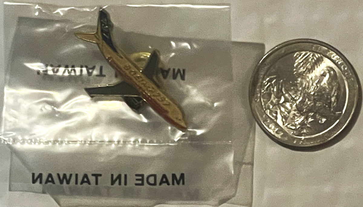 Sealed plastic bag containing brass Boeing 737 lapel pin next to British pound coin for scale comparison.