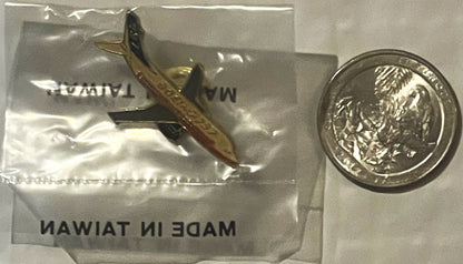 Sealed plastic bag containing brass Boeing 737 lapel pin next to British pound coin for scale comparison.