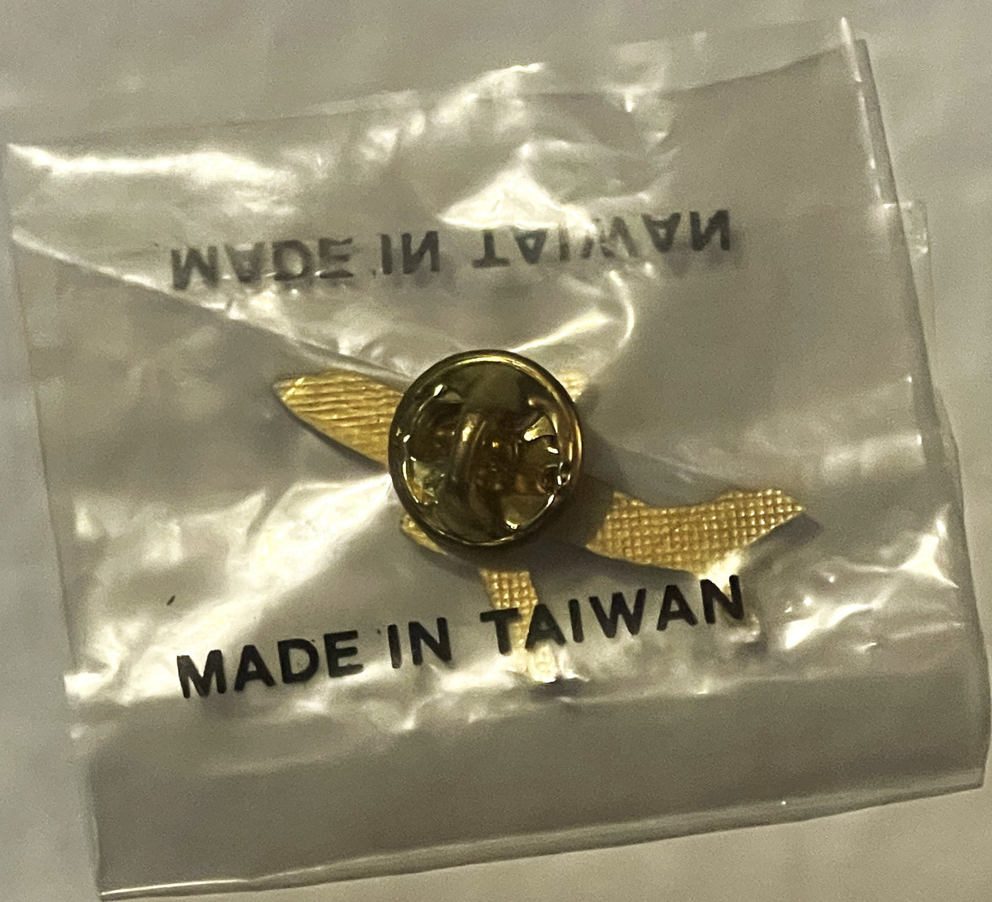 Small brass aviation lapel pin with profile portrait in clear plastic packet labeled "MADE IN TAIWAN" with gold mesh wings vi
