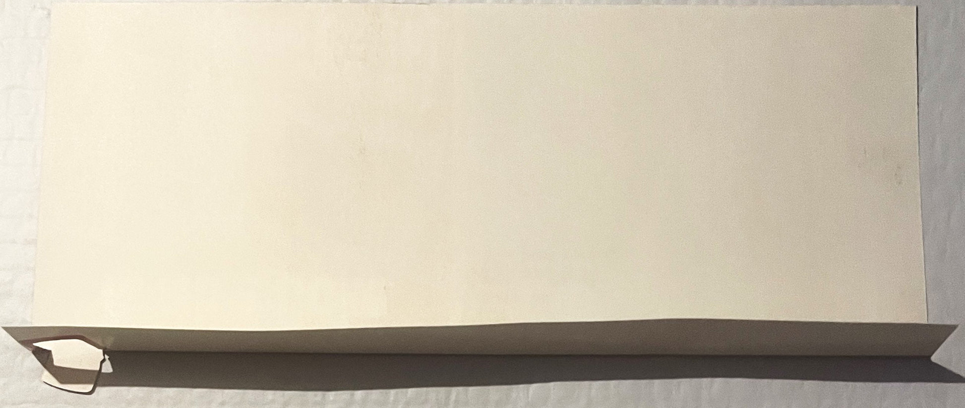Cream-colored cardboard banner with dark gray curved bottom edge and small cutout detail on left side, displayed at angle