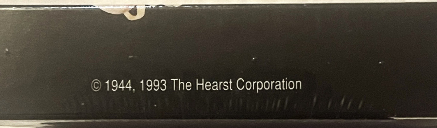 Close-up of sealed box bottom showing copyright text "© 1944, 1993 The Hearst Corporation" on dark background with tape at to