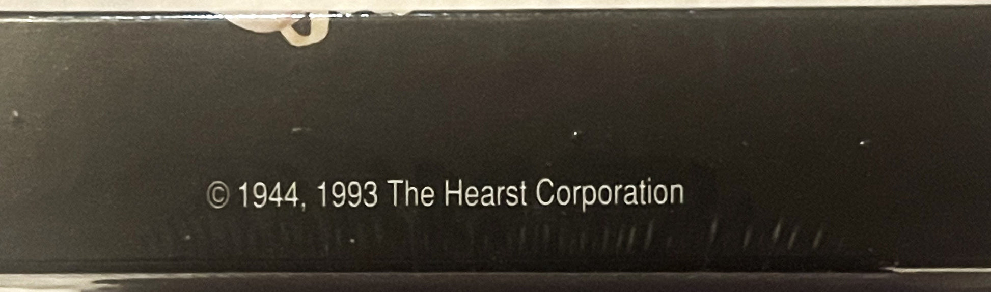 Close-up of sealed box bottom showing copyright text "© 1944, 1993 The Hearst Corporation" on dark background with tape at to