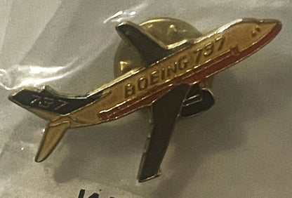 Brass and enamel Boeing 737 lapel pin with red fuselage stripe, shown at an angle against a gray background