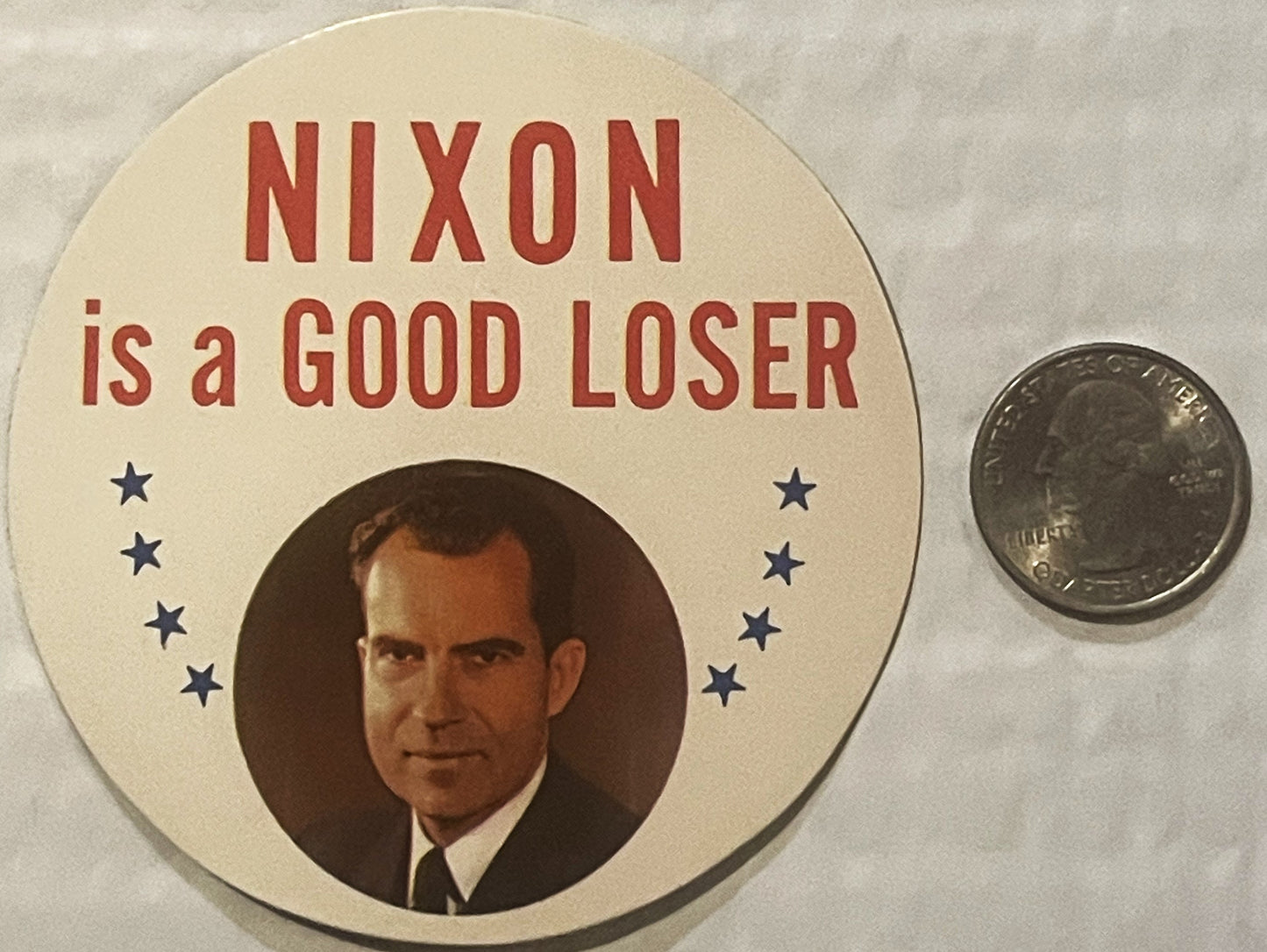 Vintage political sticker with "NIXON is a GOOD LOSER" text, portrait photo, and stars, displayed next to a quarter for scale