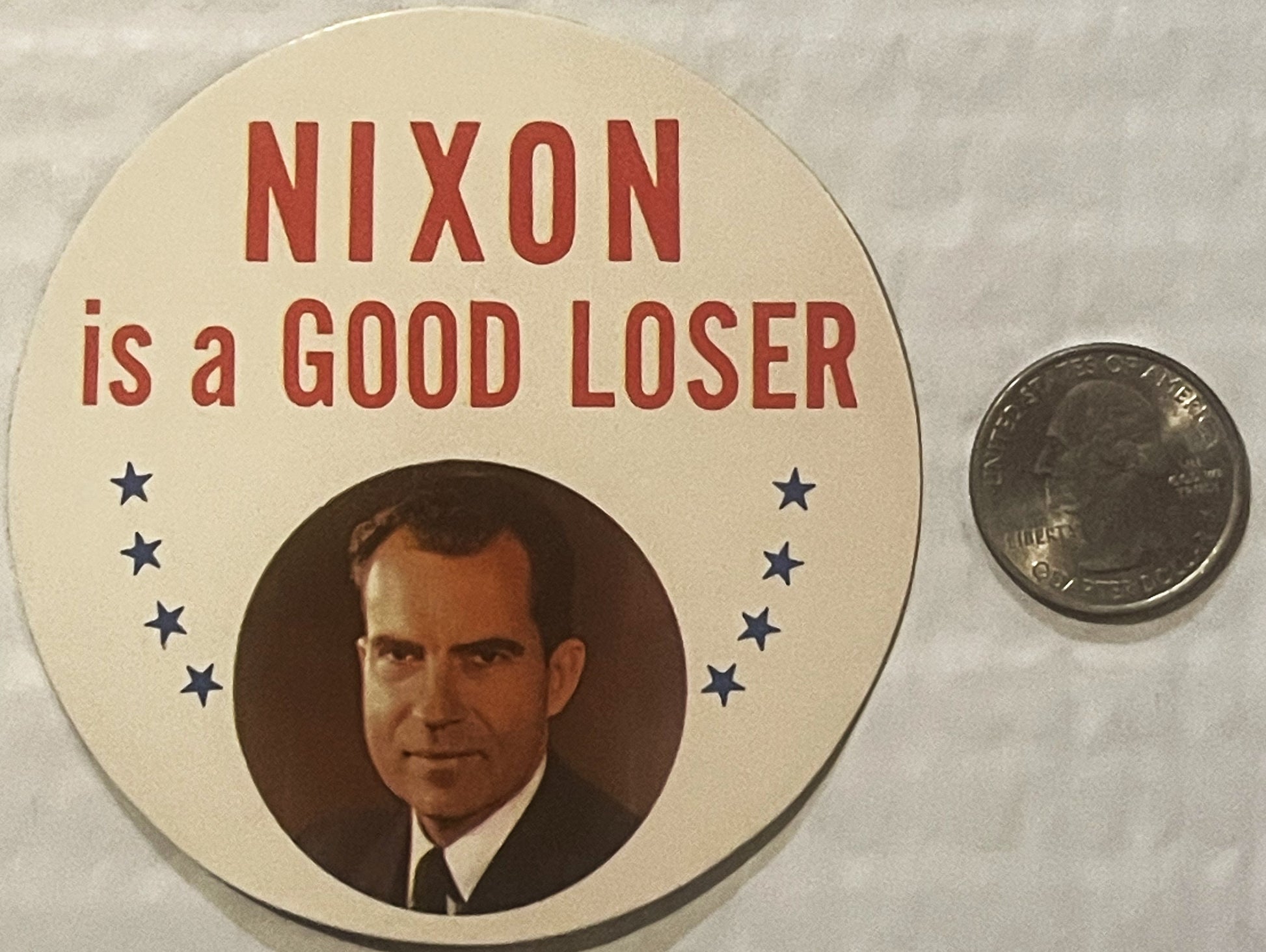 Vintage political sticker with "NIXON is a GOOD LOSER" text, portrait photo, and stars, displayed next to a quarter for scale