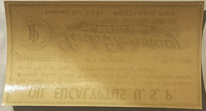 Tan paper label with embossed text and white tape strip on lower left edge, photographed flat against white background