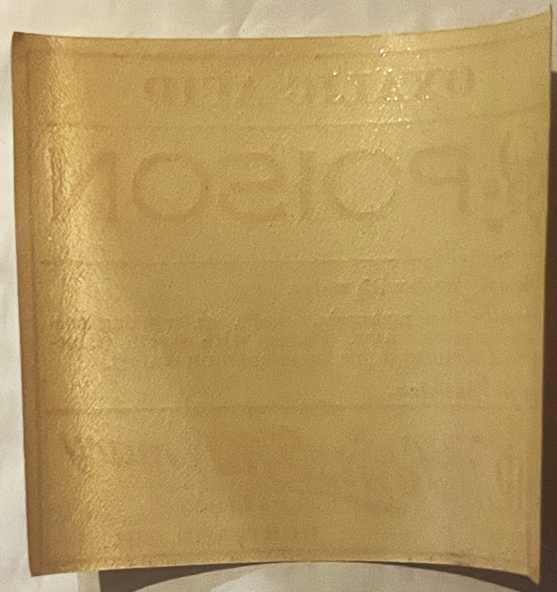 Curved tan paper label with embossed text, photographed flat against white background showing wear and creasing on surface