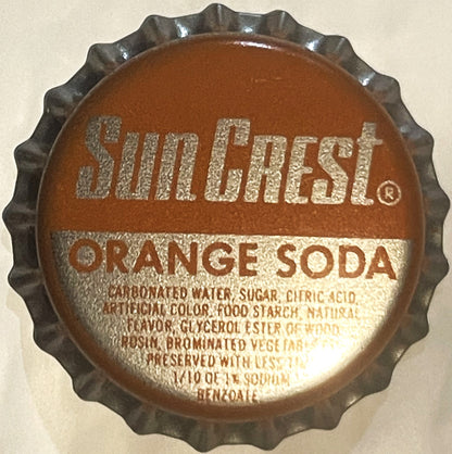 Vintage Sun Crest Orange Soda bottle cap with ridged metal edges, embossed text on brown and cream colored surface against be