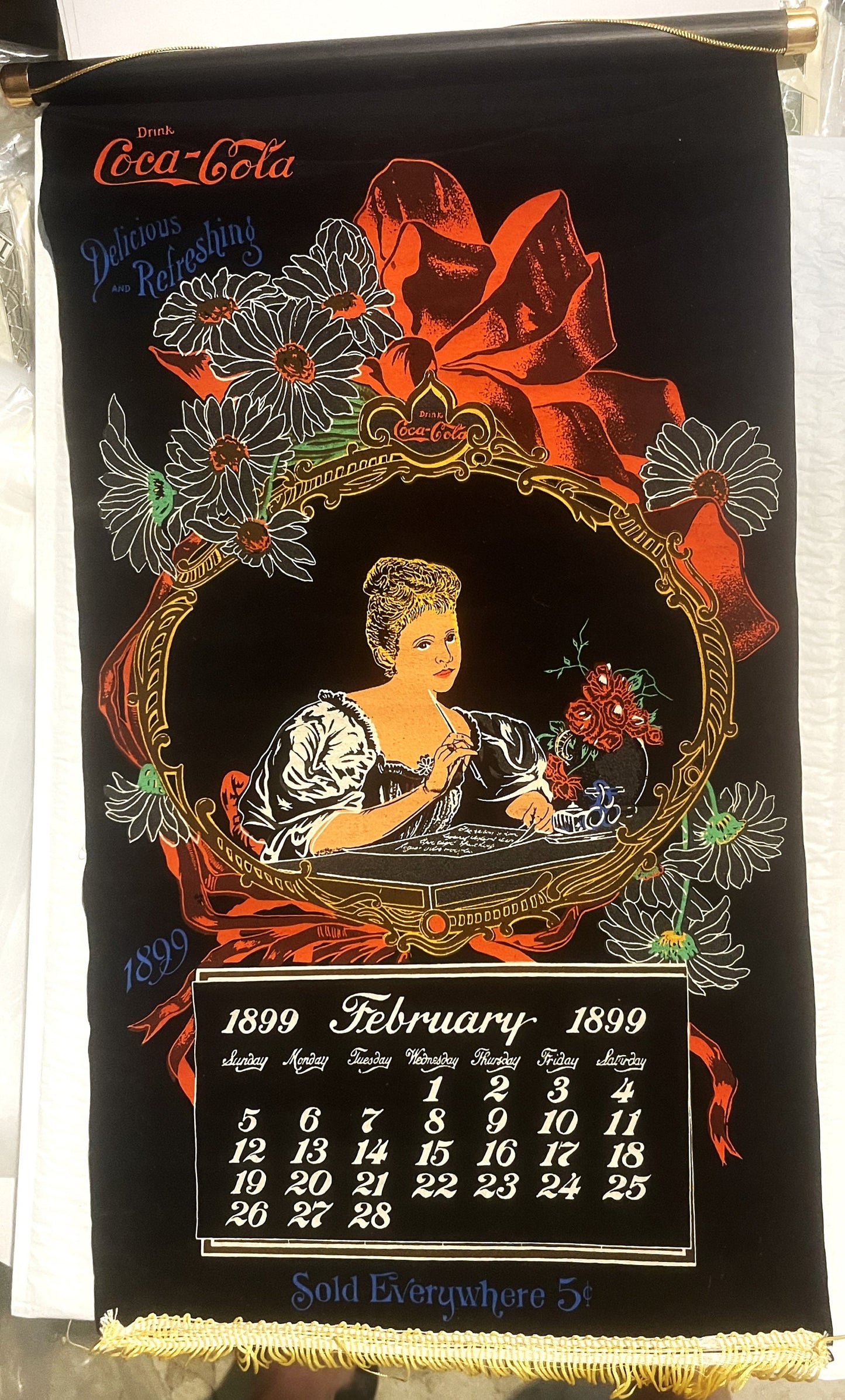 Antique Coca-Cola cloth calendar scroll for February 1899 with ornate gold frame, woman portrait, flowers, and red ribbon on 