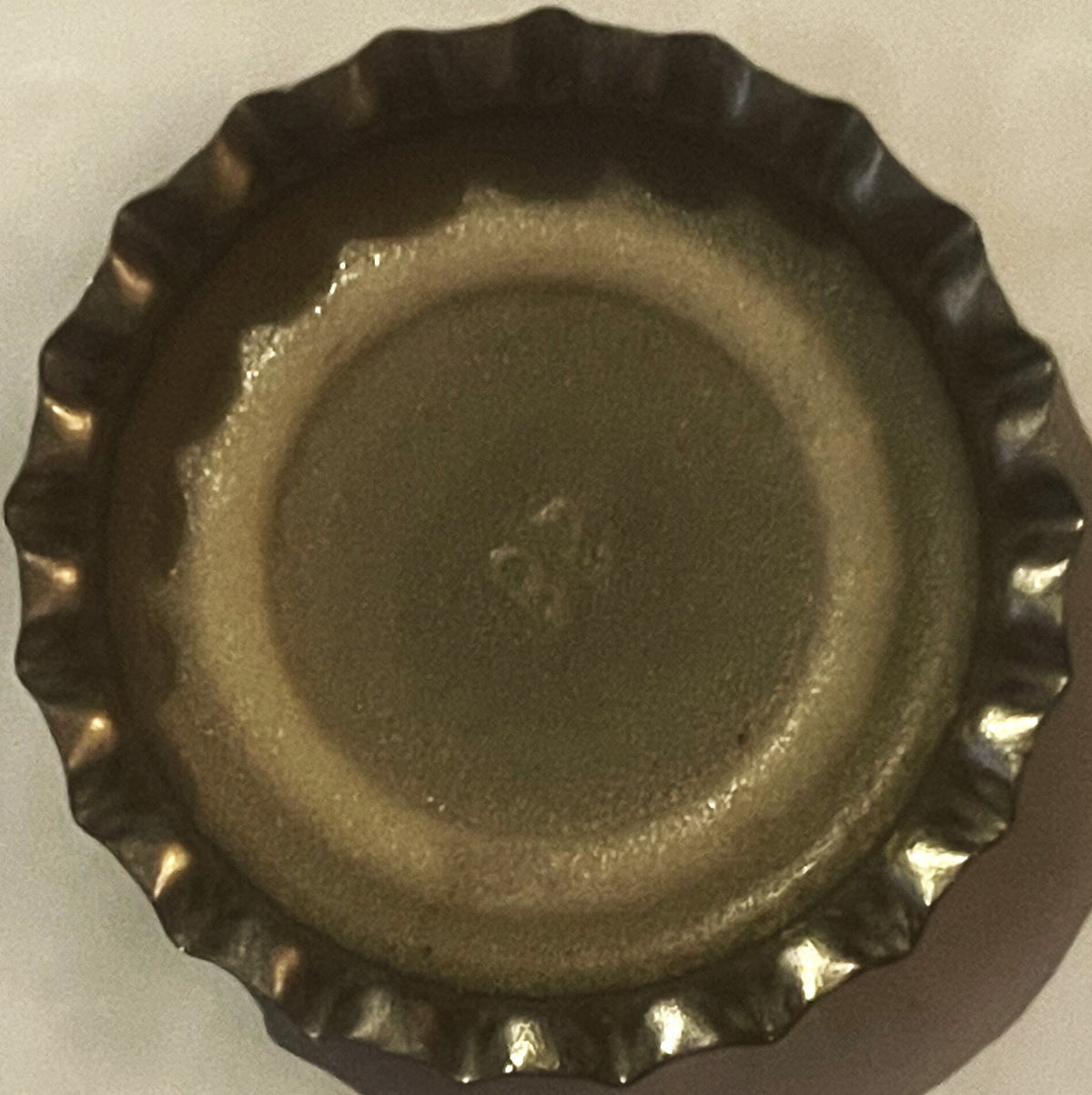 Vintage bottle cap with ridged metal edges and textured center, photographed from above against a light background