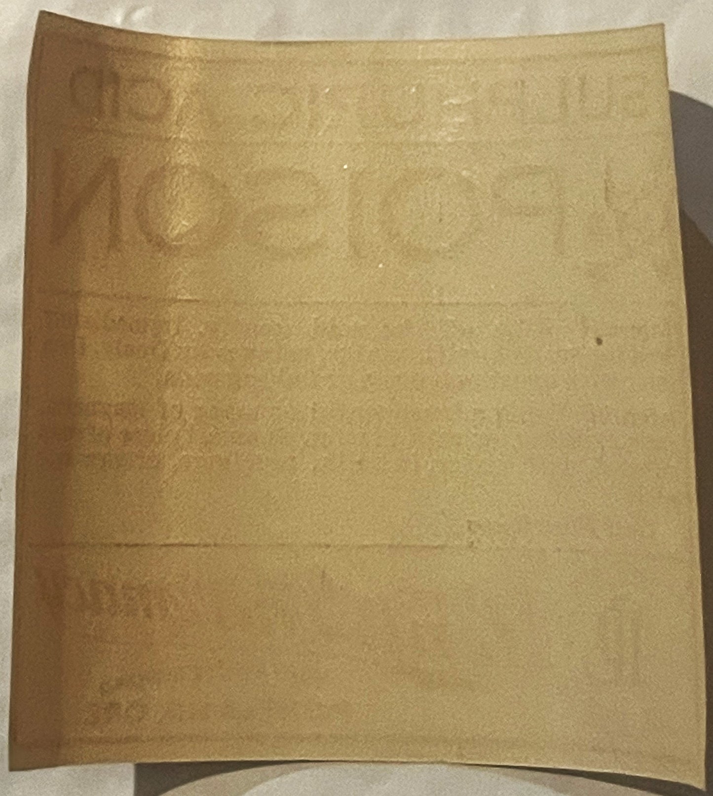 Aged tan paper label with curved edges, photographed flat against white background, showing wear and faint markings but text 