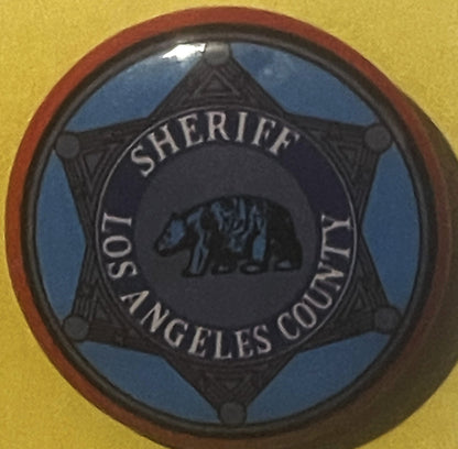 Circular tin litho badge with blue and black star design reading "Los Angeles County Sheriff" with bear emblem, mounted on ye