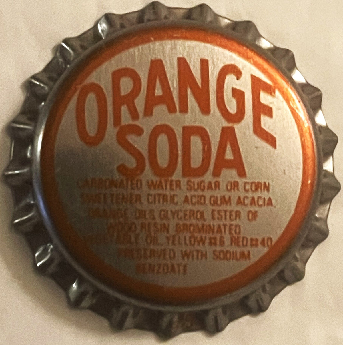 Vintage Orange Soda bottle cap with corrugated metal edges and orange and white label on beige background