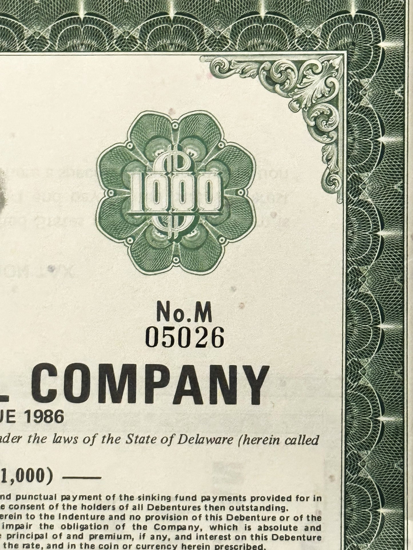 Close-up of a green and cream bond certificate showing ornate scrollwork border, 1000 denomination in floral seal, "No.M 0502
