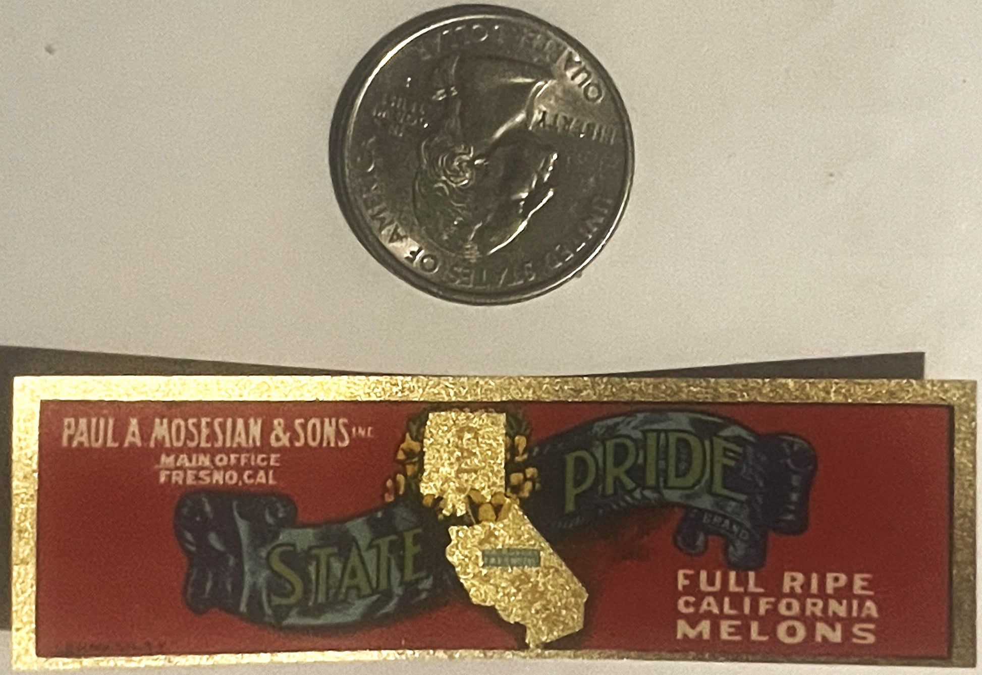 Vintage California State Pride melon label next to a quarter for scale, showing red background with gold state outline and te