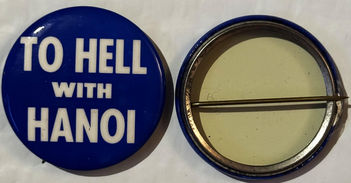Front and back of a blue pinback button reading "TO HELL WITH HANOI" in white capital letters, with metal clasp visible on re