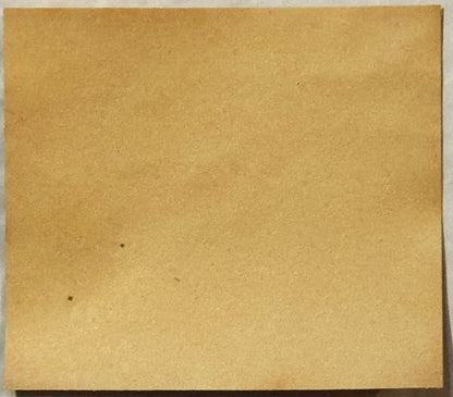 Tan cardboard backing or label sheet with minor dark spots and creasing, photographed flat against white background