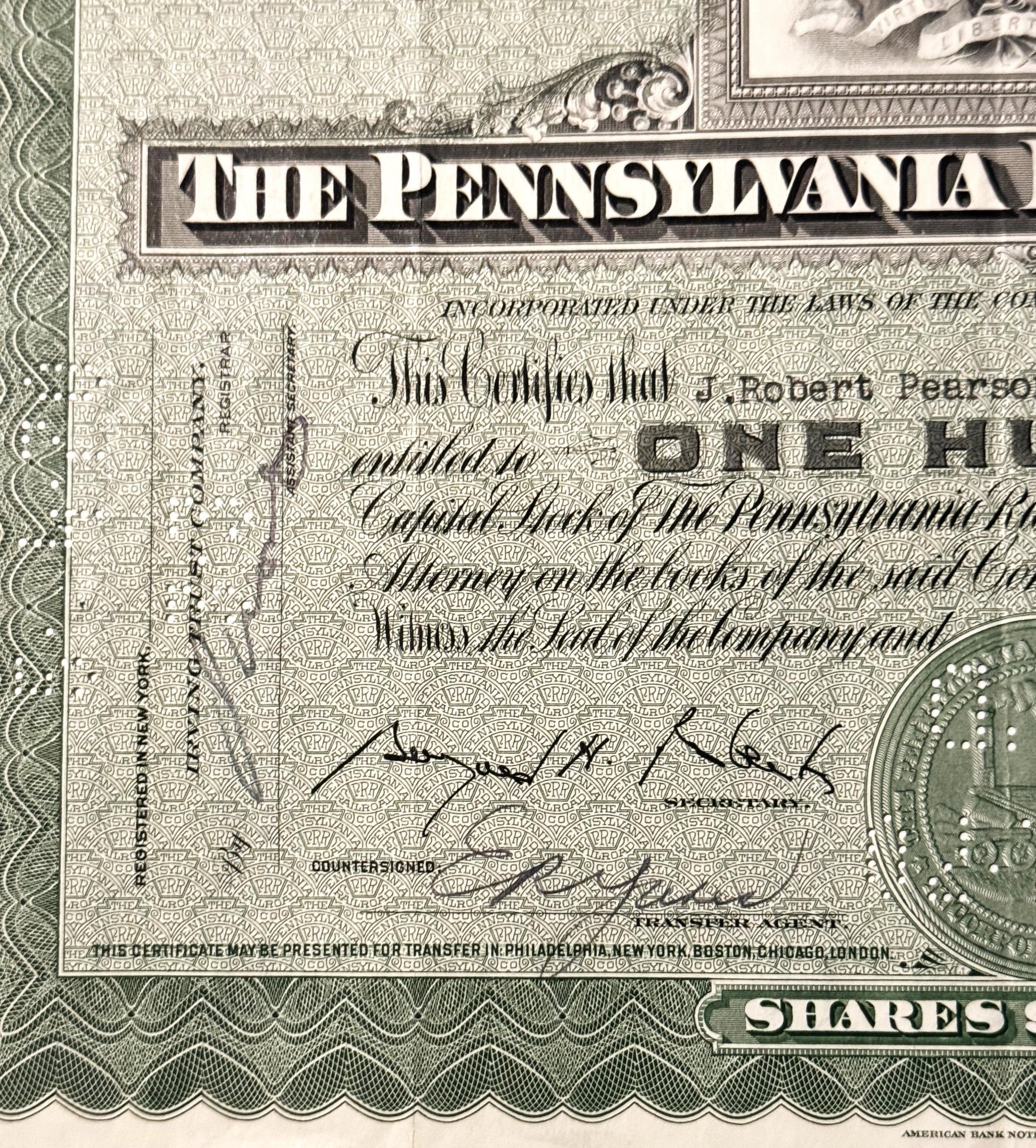 Close-up of vintage Pennsylvania Railroad stock certificate with ornate border, cursive signatures, and partial coin visible 