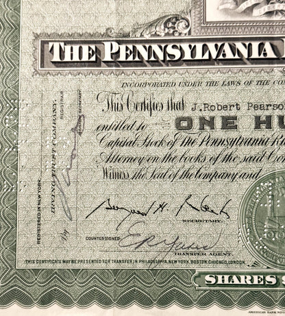 Close-up of vintage Pennsylvania Railroad stock certificate with ornate border, cursive signatures, and partial coin visible 
