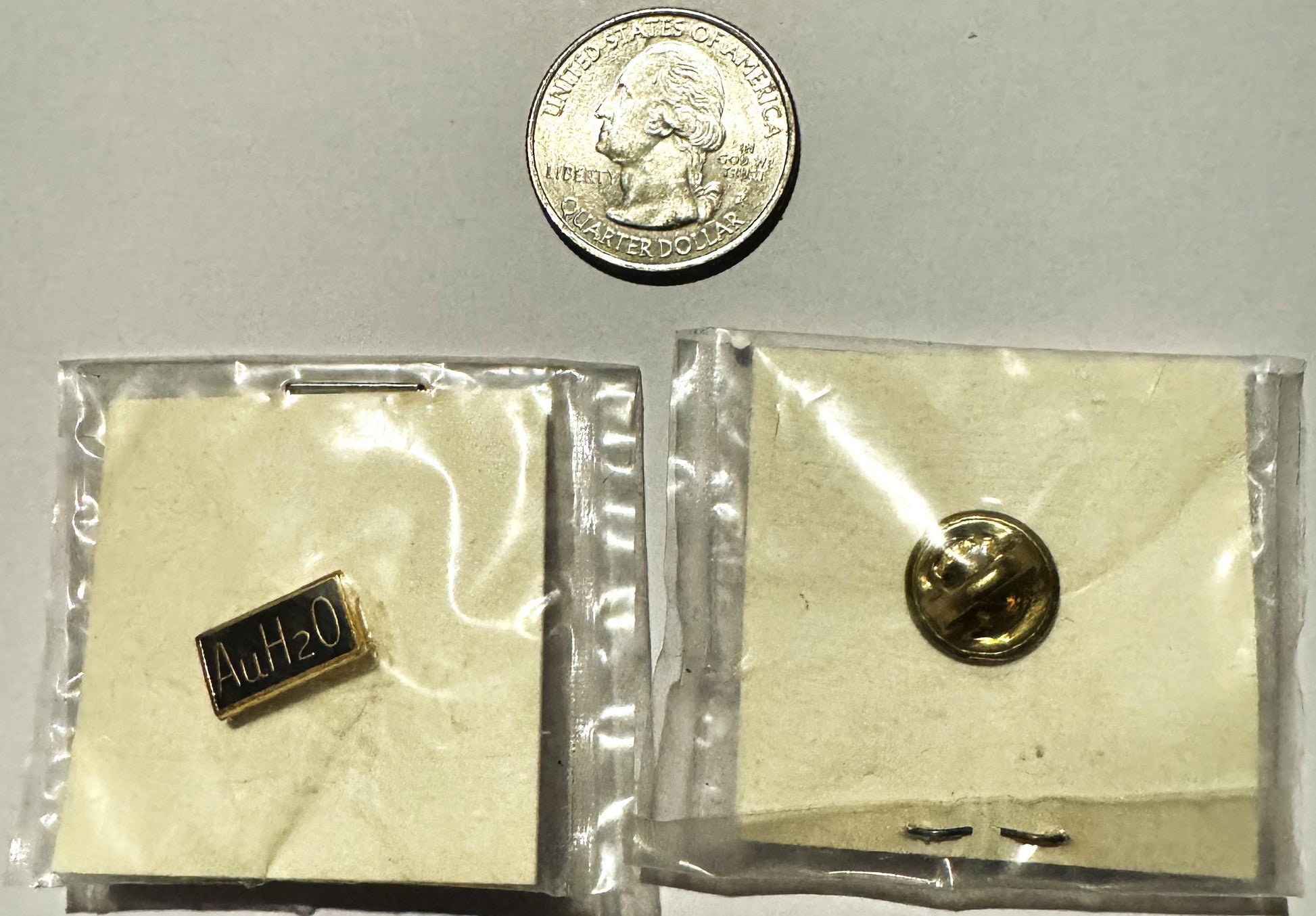 Vintage AuH2O Goldwater campaign pin in sealed plastic bag with quarter for scale, showing small gold button and rectangular 