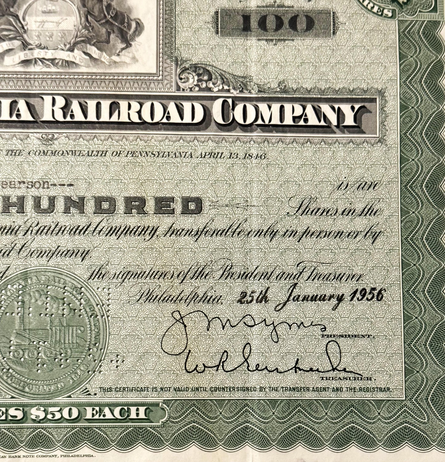 Close-up of vintage Pennsylvania Railroad Company stock certificate showing "100" denomination, ornate border design, officia