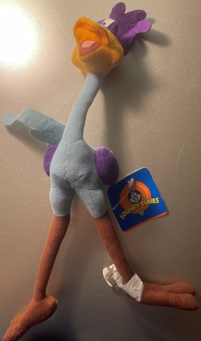 Vintage Road Runner plush toy with orange head, gray body, purple wings and feet, orange legs, displayed against beige wall w