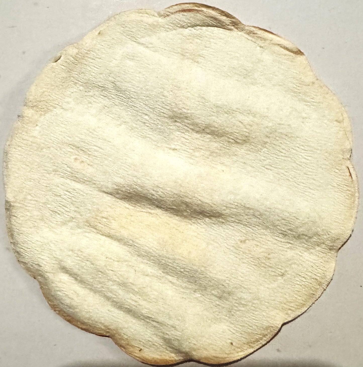 Cream-colored circular cloth coaster with embossed diagonal ridged texture pattern and darkened edges, photographed flat agai