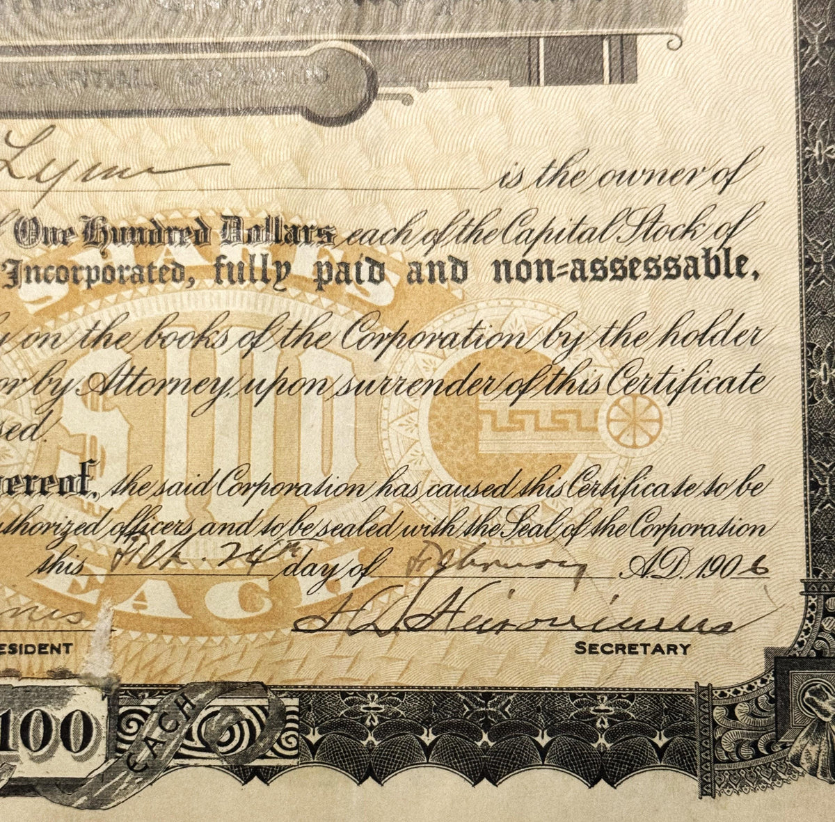 Close-up of stock certificate showing "One Hundred Dollars" text, ornate border, and handwritten signature dated A.D. 19