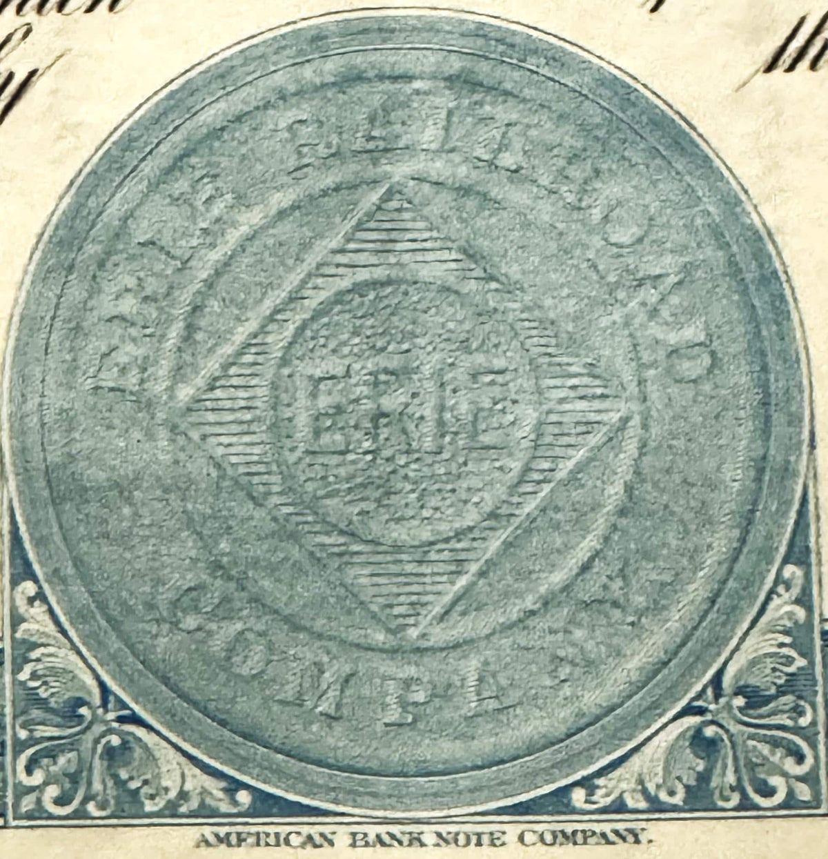 Circular vignette featuring ornate shield design with horizontal lines, surrounded by decorative blue scrollwork corners and 