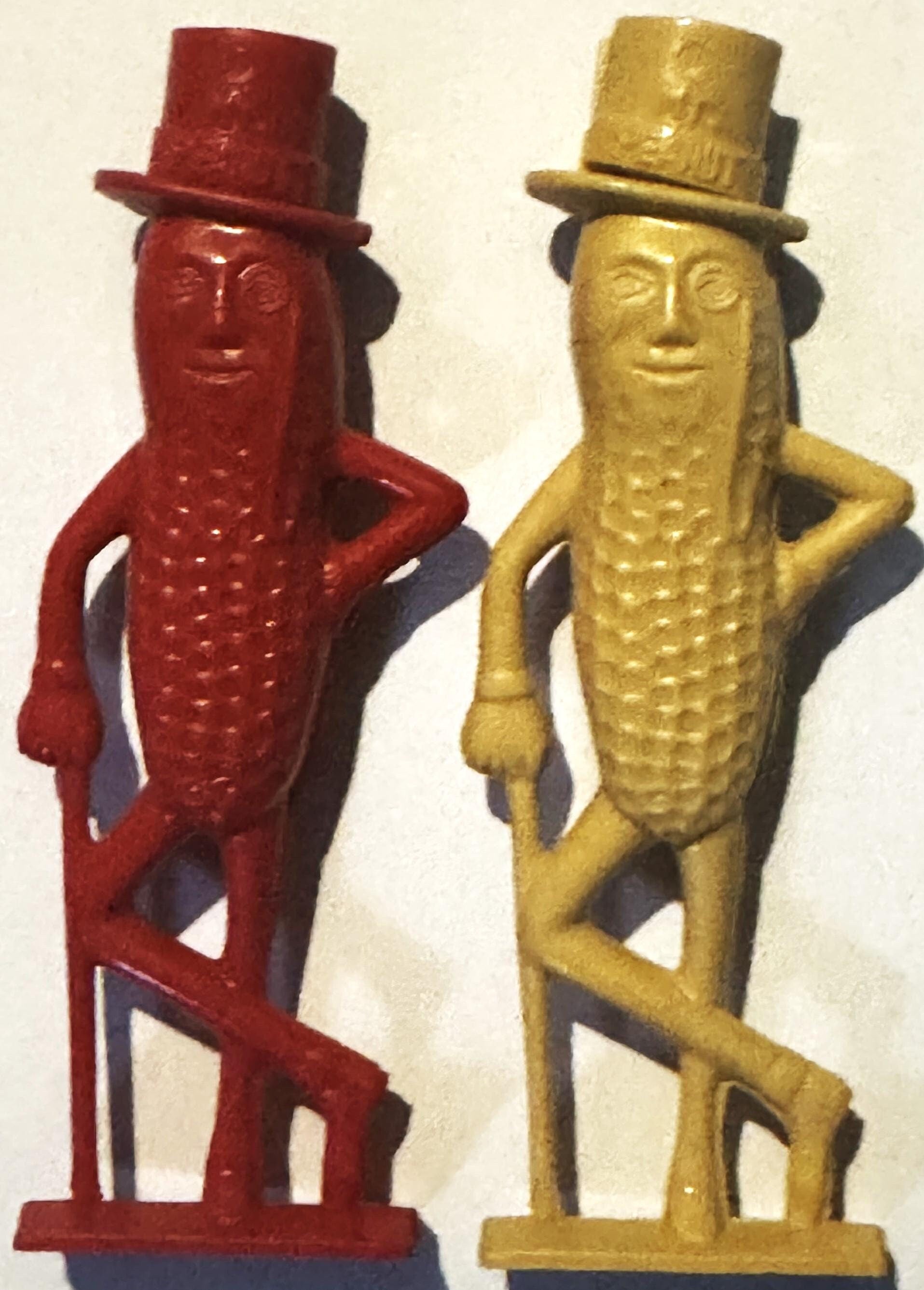 Two Mr. Peanut plastic figural whistles in red and gold, wearing top hats, shown side by side against a cream background