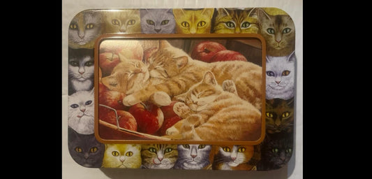 Persis Clayton Weirs lid art on the Cat Companions tin: two sleeping orange tabby cats curled in a woven apple basket, framed by a die-cut window and ringed by a wraparound cat-face portrait border.