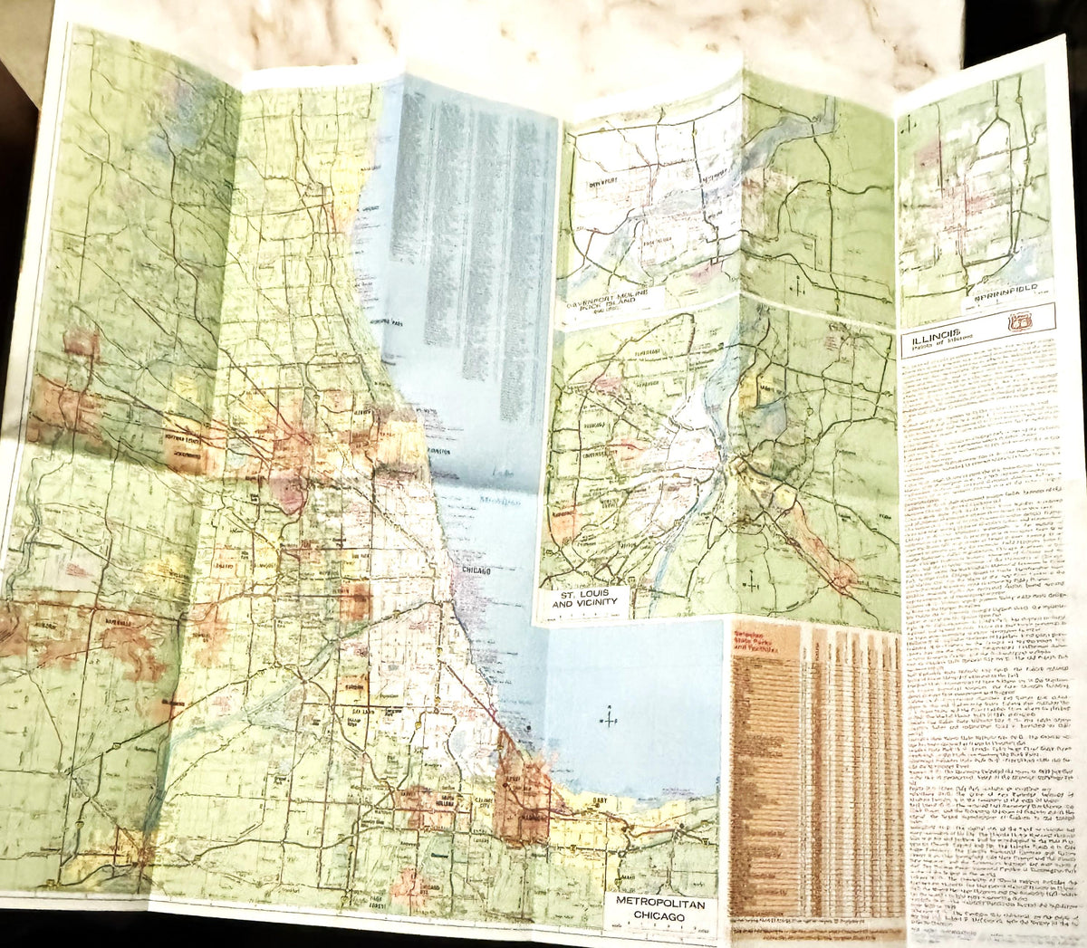 Opened vintage Route 66 Illinois map with green and tan coloring, Chicago area detail, and informational text pages visible o