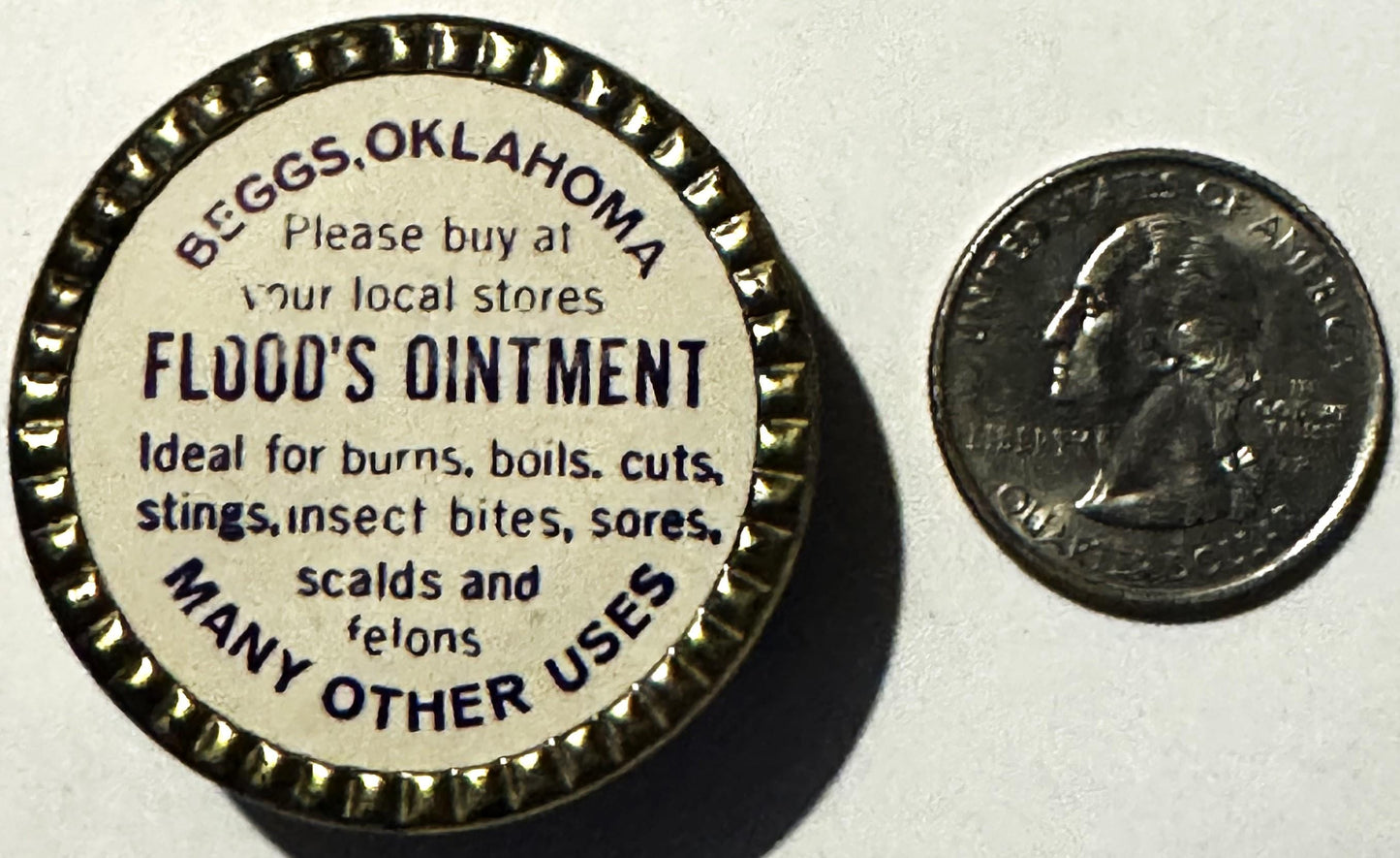 Vintage Flood's Ointment tin from Beggs, Oklahoma next to a quarter for scale, showing cream-colored label with dark text lis