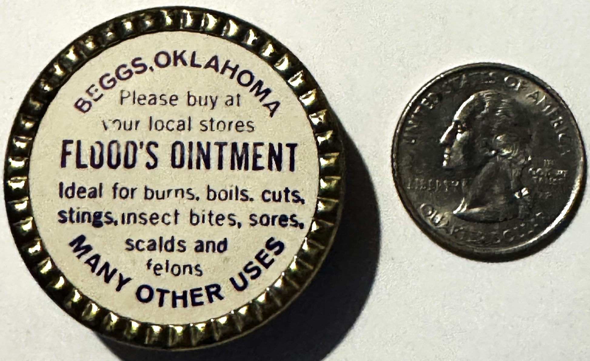 Vintage Flood's Ointment tin from Beggs, Oklahoma next to a quarter for scale, showing cream-colored label with dark text lis