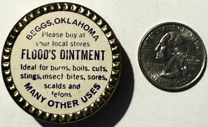 Vintage Flood's Ointment tin from Beggs, Oklahoma next to a quarter for scale, showing cream-colored label with dark text lis