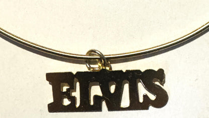 Black metal "ELVIS" nameplate charm hanging from gold-tone choker necklace against cream background