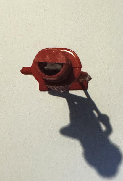 Red plastic Mr. Peanut figural whistle held in a hand against white wall, casting dark shadow