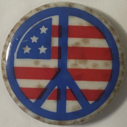 Vintage peace symbol pin with American flag background in blue, red, and white on weathered metal backing