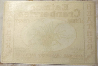 Cream-colored vintage cranberry barrel label with faded embossed text and decorative border, photographed flat against light 