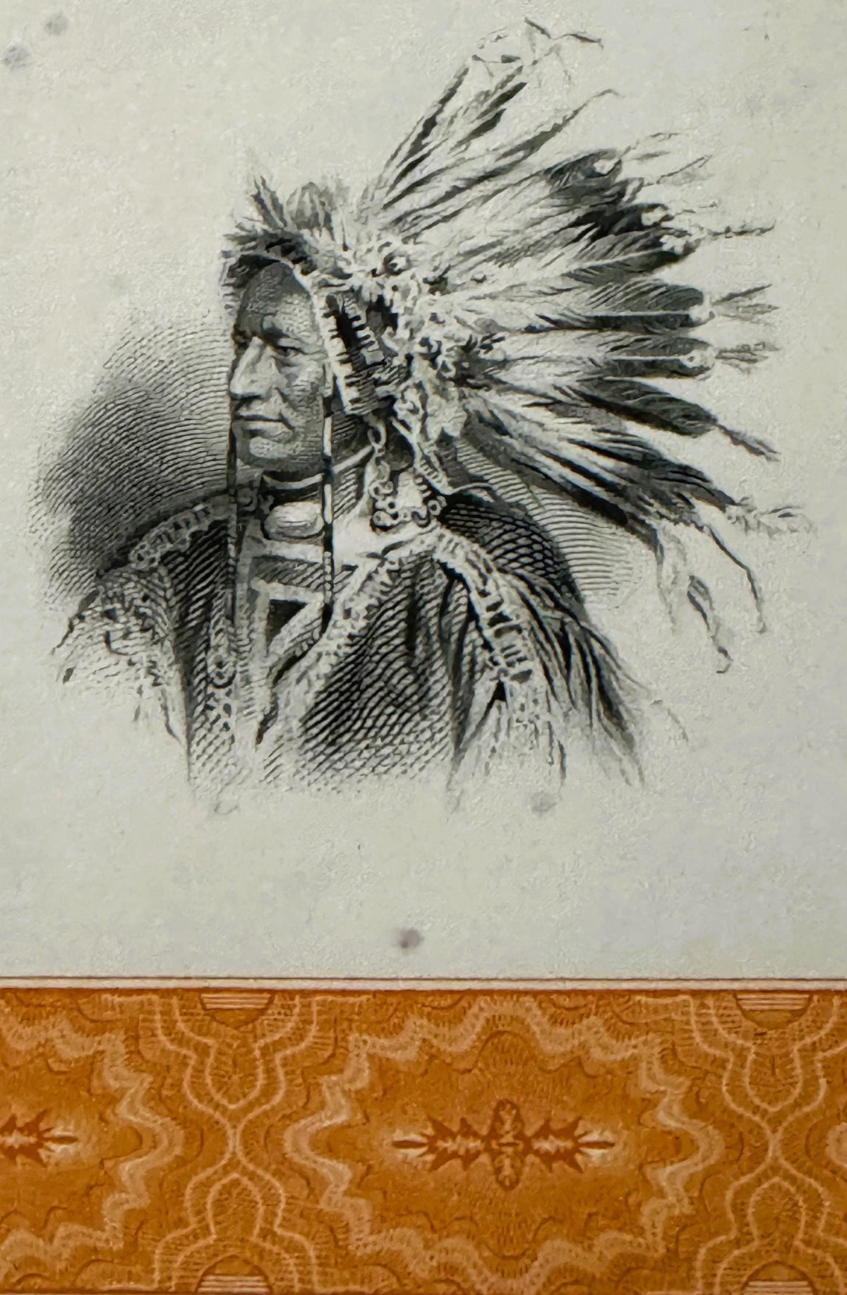 Engraved vignette of a Native American chief wearing an elaborate feathered headdress and decorated clothing, printed in blac