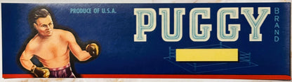 Vintage fruit crate label with boxer in boxing gloves on dark blue background, large "PUGGY" text, yellow rectangular panel, 