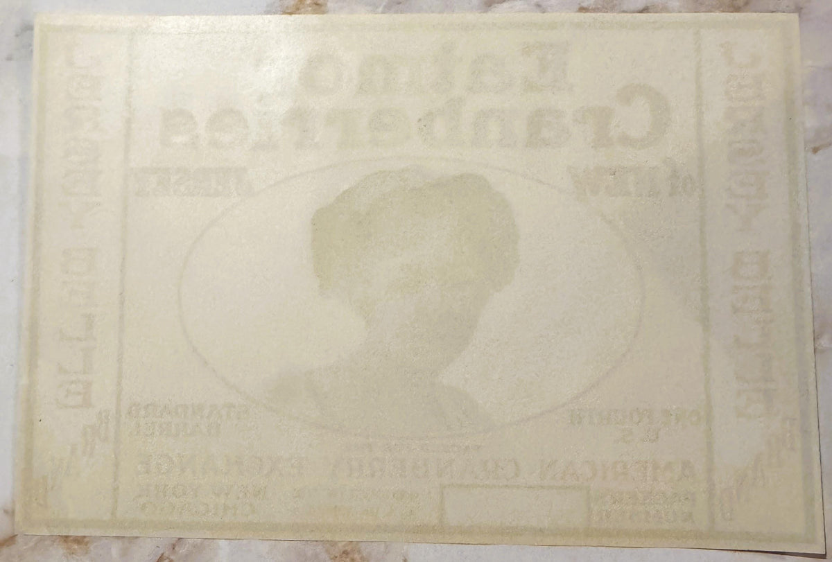 Cream-colored vintage cranberry barrel label with faded embossed design showing a profile portrait in center, text visible ar