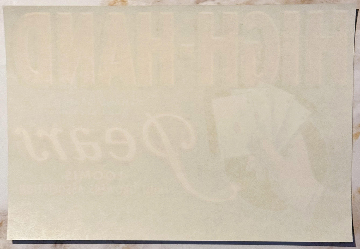 Cream-colored vintage crate label with faint watermarked design featuring playing cards and text, shown flat against neutral 