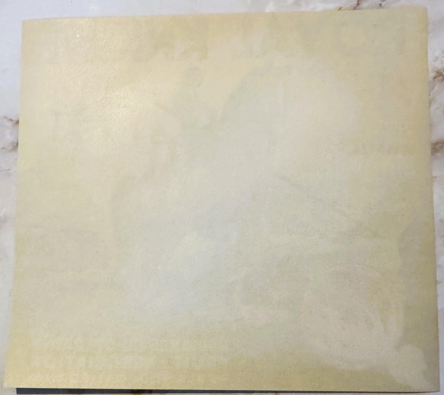 Cream-colored vintage citrus crate label with faint printed text, photographed flat against white marble surface