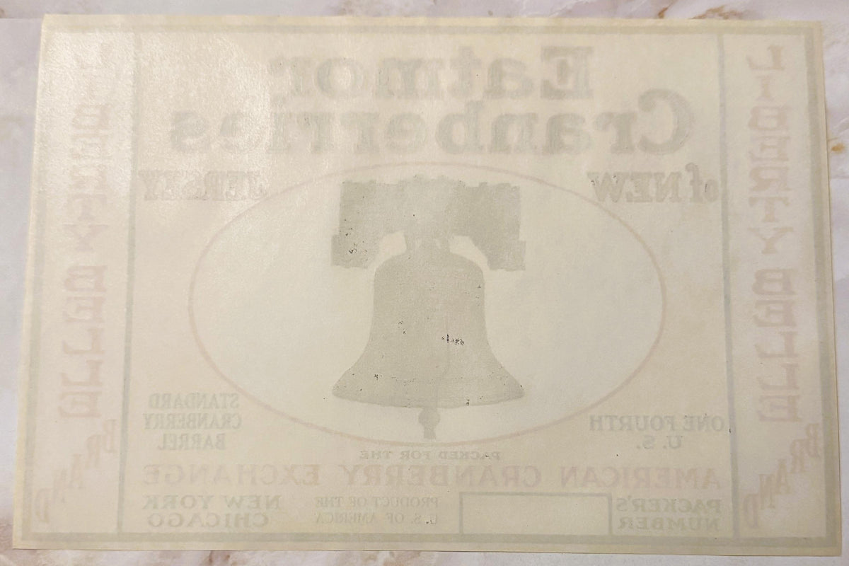 Faded cream-colored vintage cranberry barrel label featuring embossed Liberty Bell in oval frame, text largely illegible due 