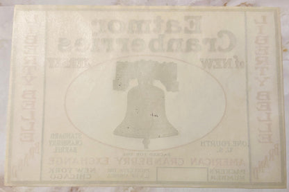 Faded cream-colored vintage cranberry barrel label featuring embossed Liberty Bell in oval frame, text largely illegible due 