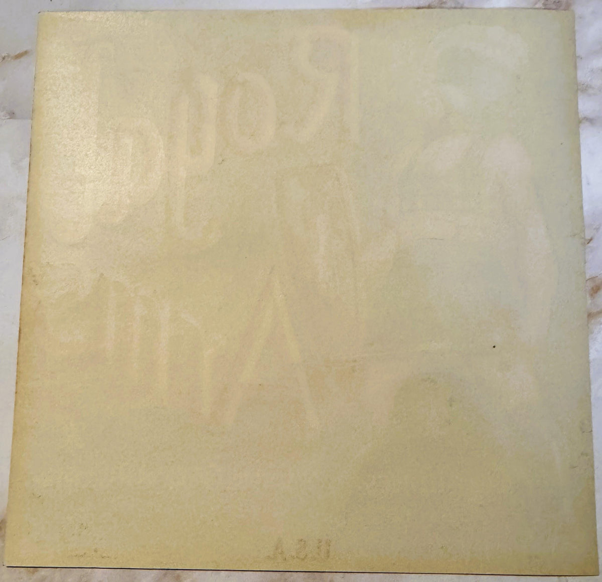 Cream-colored vintage crate label with embossed Royal Arms design and faint text, photographed flat on marble surface